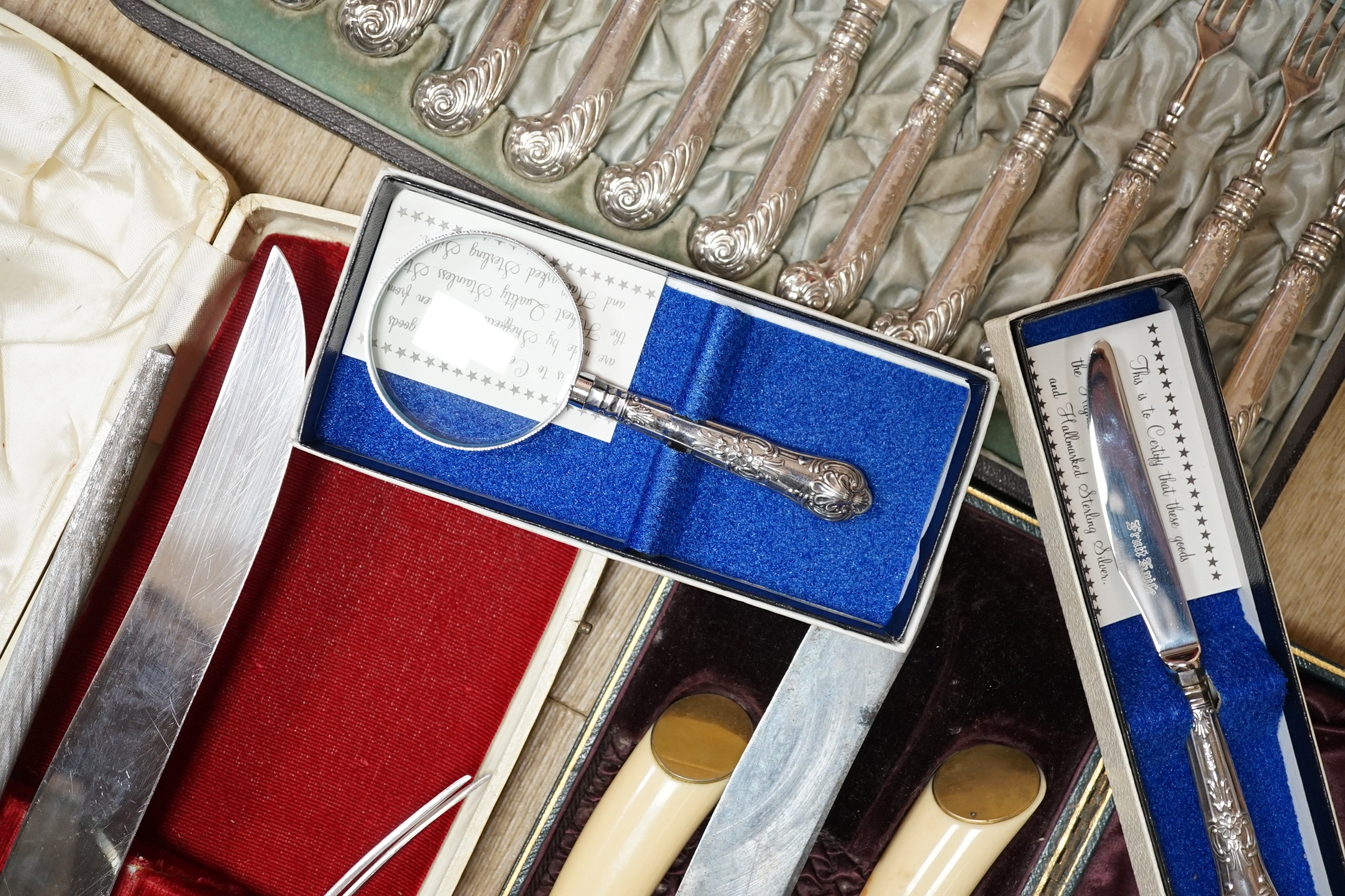 Two cased plated carving sets, a cased set of silver handled cake knives, a modern silver handled magnifying glass and cake slice.